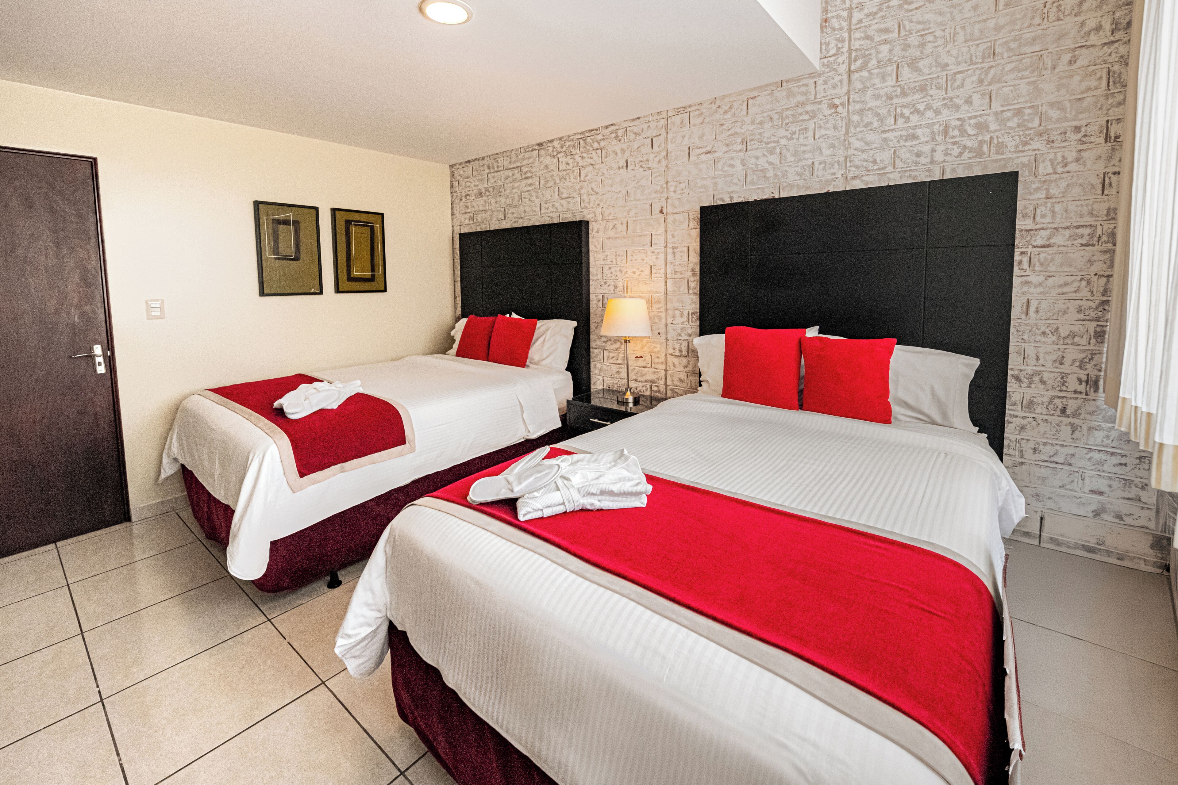 A hotel room with two beds, a brick wall, and a door.