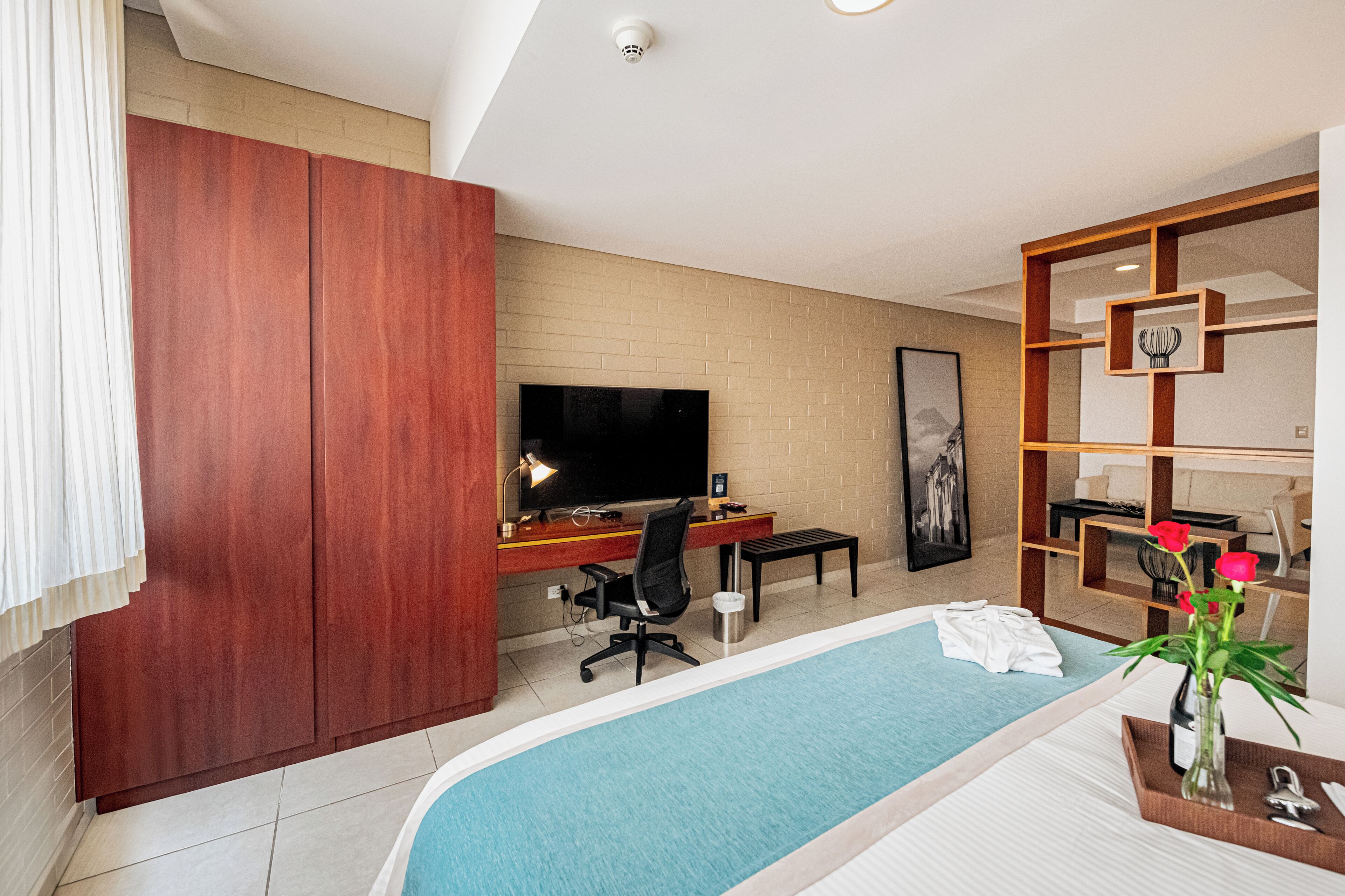 Habitación de hotel con armario de madera, escritorio con computadora, televisor, piscina pequeña y repisa de madera con adornos.