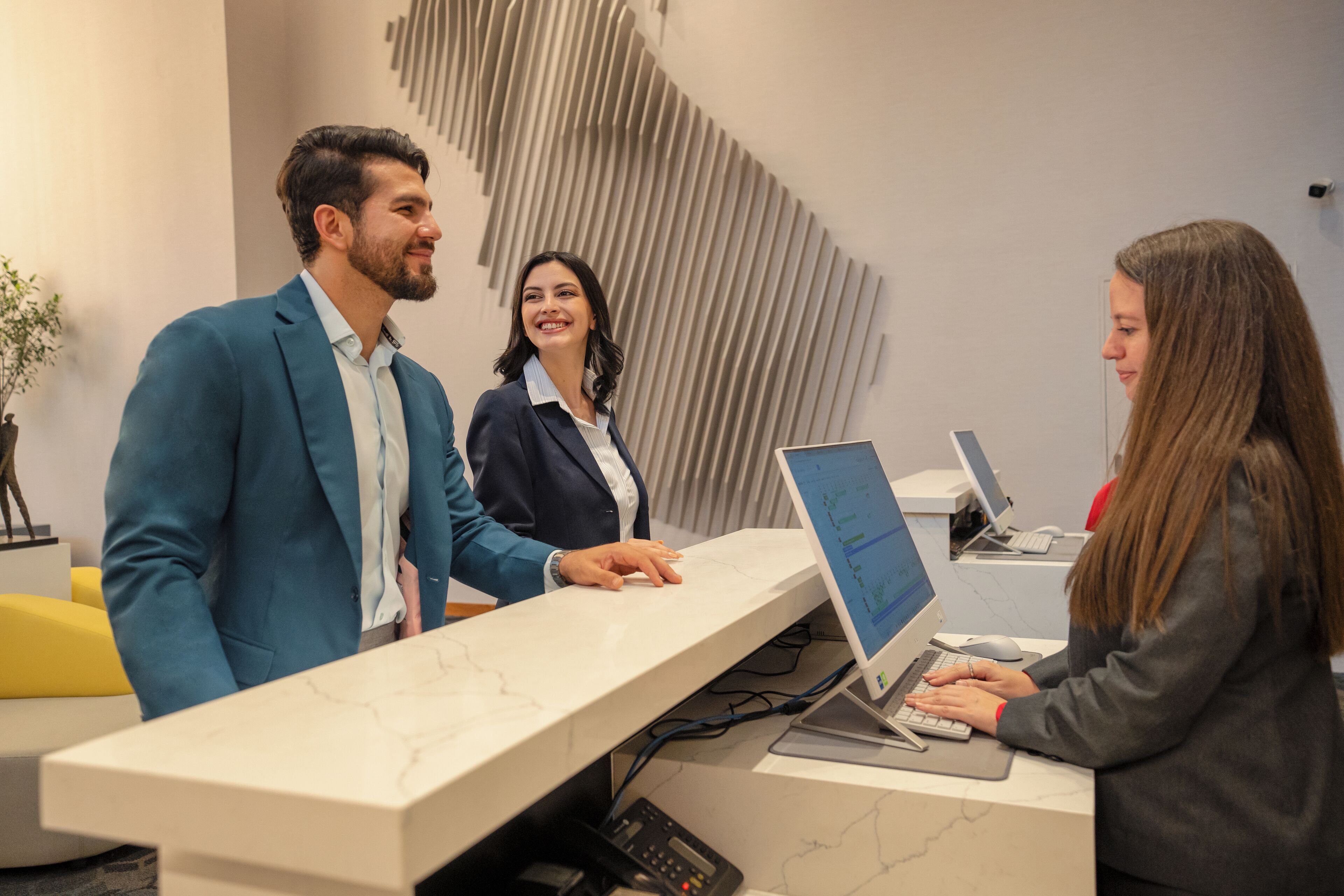 A reception desk with a modern design, a computer, and a person working on a laptop.