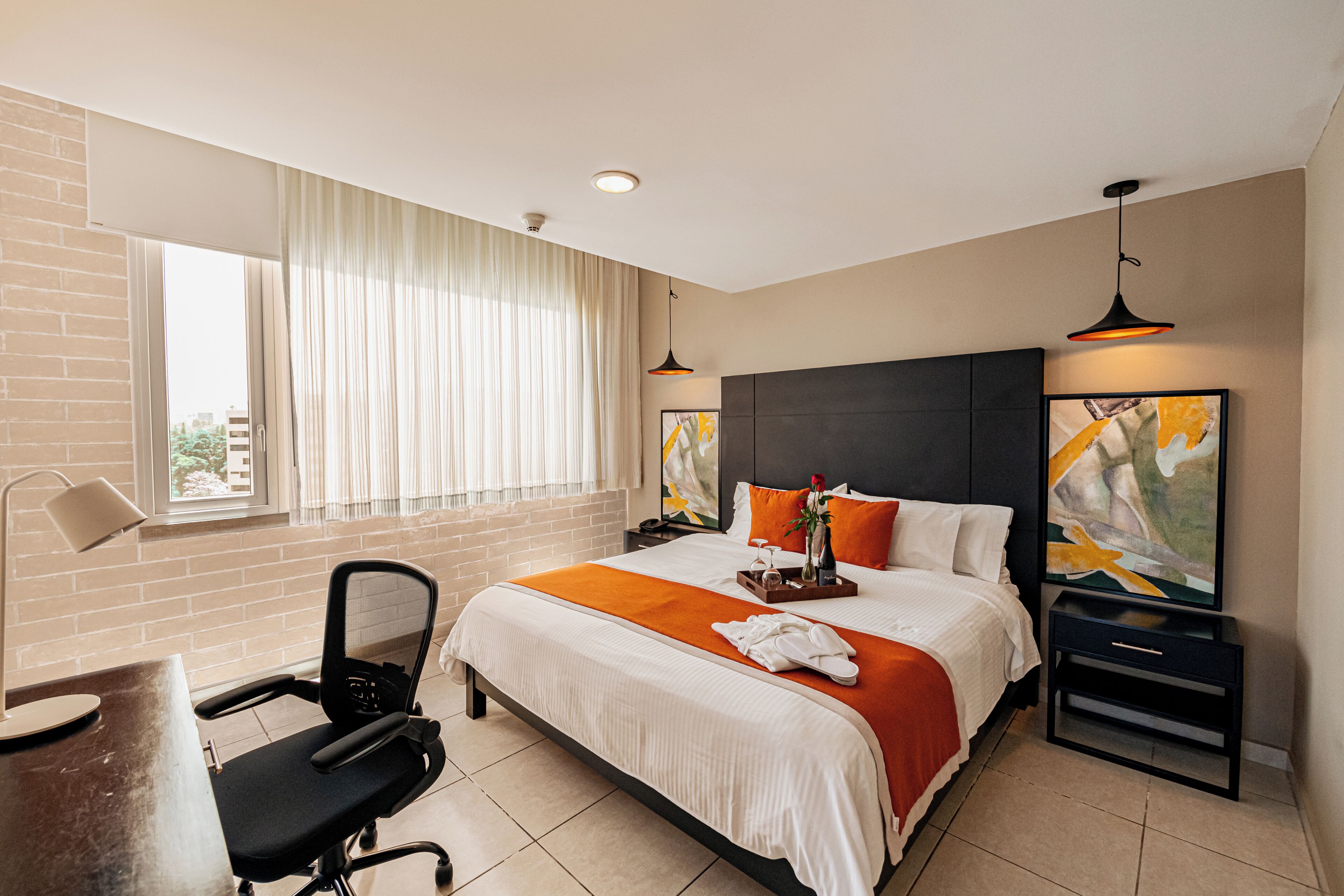A hotel room with a bed, desk, chair, and artwork on the walls.