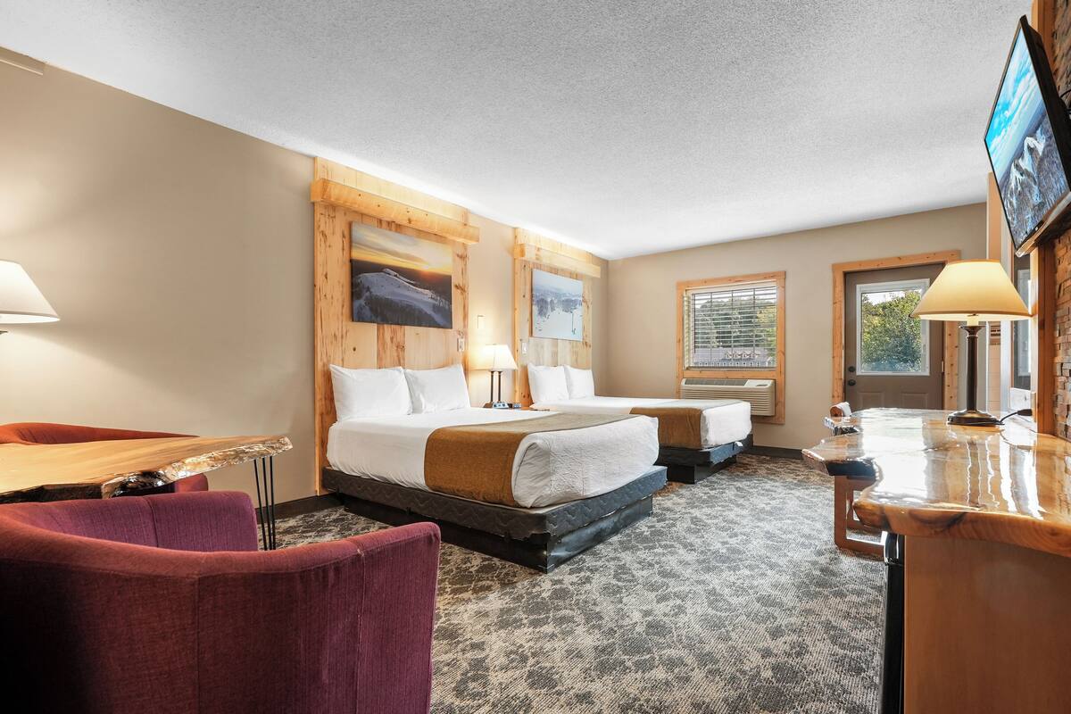A hotel room with two beds, a desk, a chair, and a TV mounted on the wall.