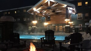 A heated outdoor pool area with a fire pit, surrounded by snow-covered chairs and a covered seating area. - Caberfae Peaks Ski & Golf Resort (Cadillac)