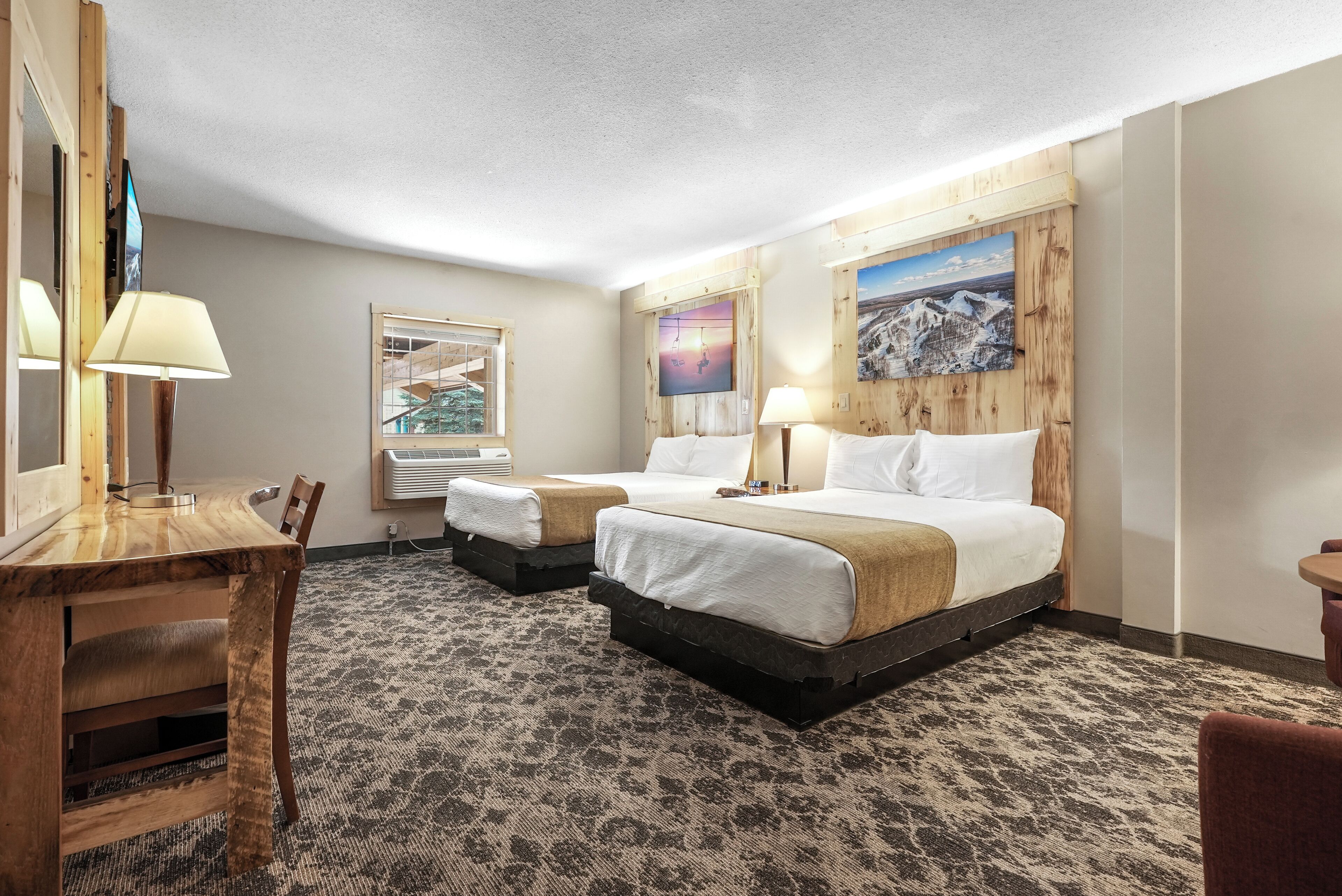 Ein Hotelzimmer mit zwei Betten, einem Holztisch, einem Stuhl, einem Fernseher und Kunstwerken an den Wänden.