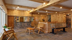 A spacious room with wooden walls and a stone fireplace. There is a wooden bench and a table with chairs. - Caberfae Peaks Ski & Golf Resort (Cadillac)