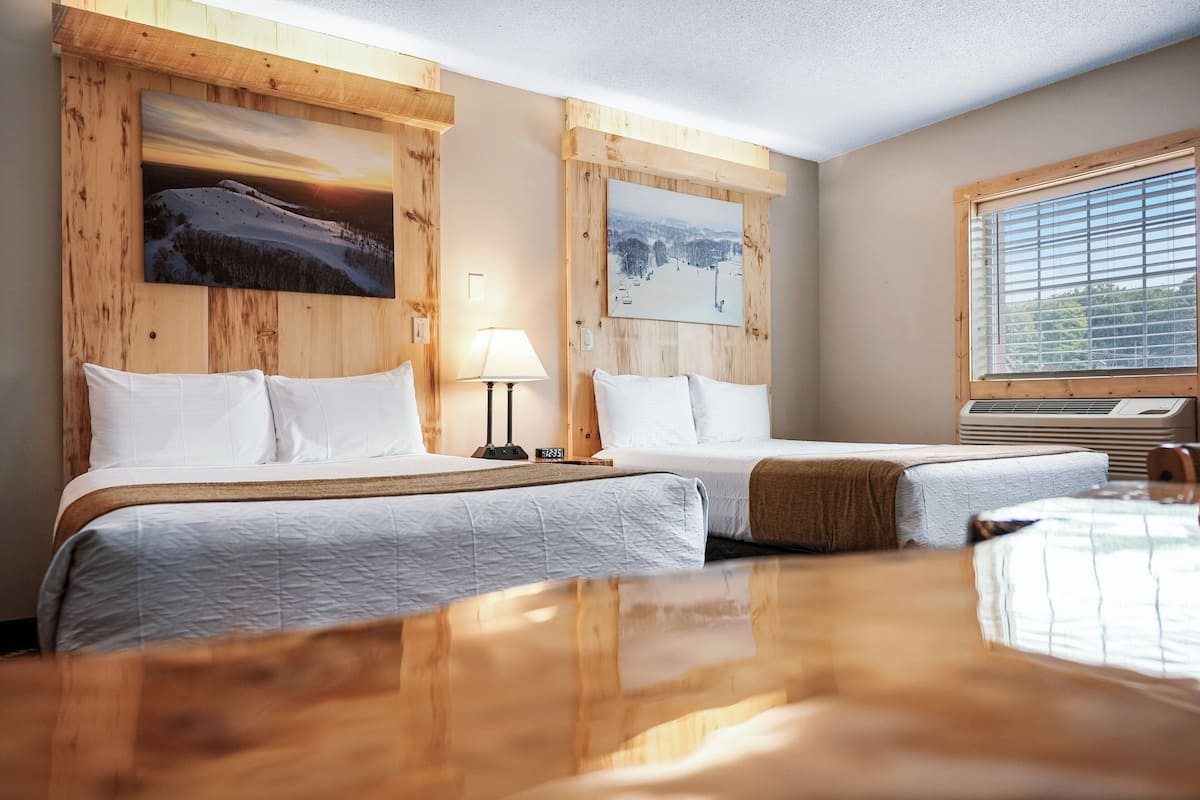 A hotel room with two beds, wooden paneling, a large window, and two paintings on the walls.