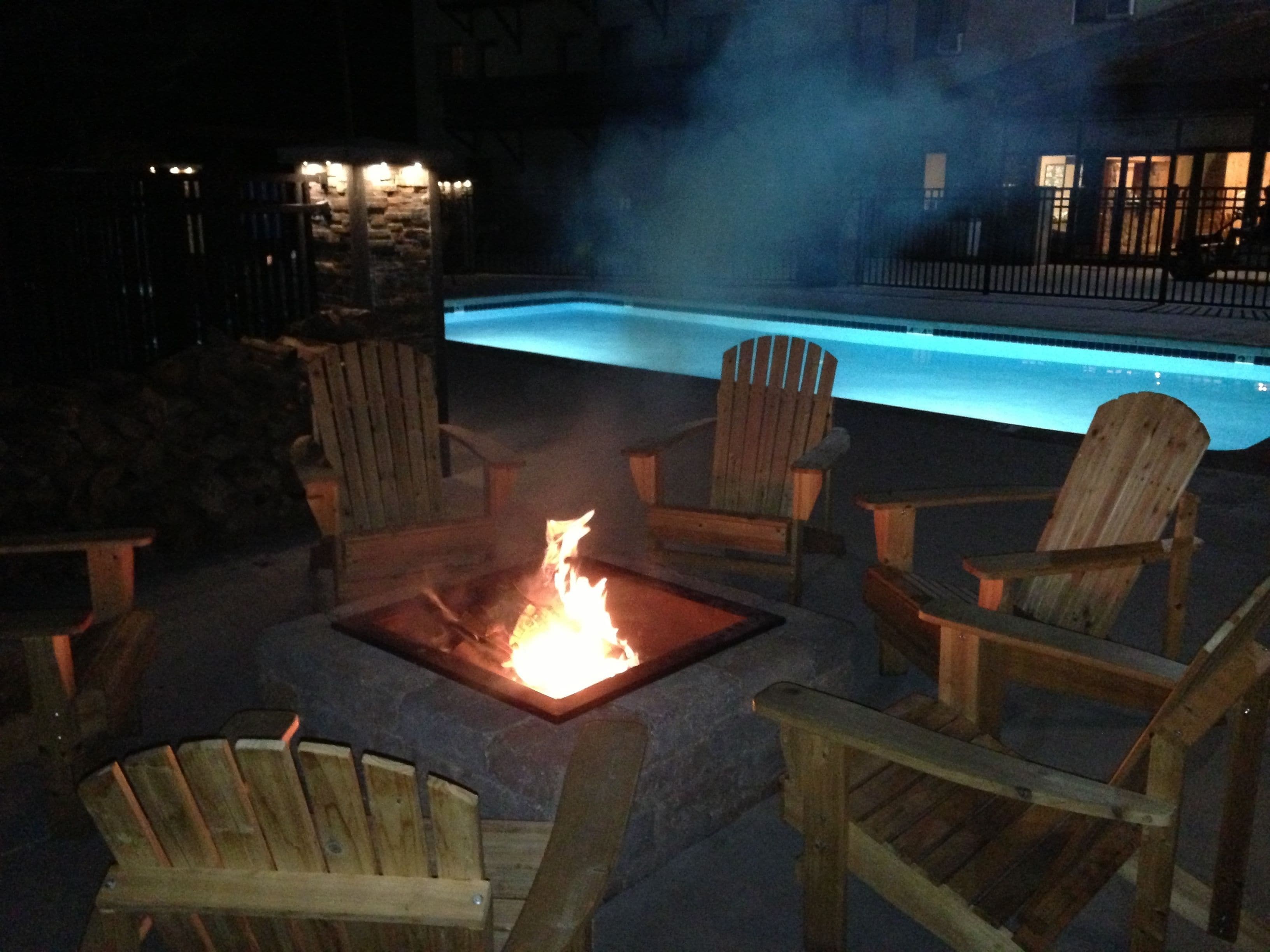 A poolside area with a fire pit and Adirondack chairs.