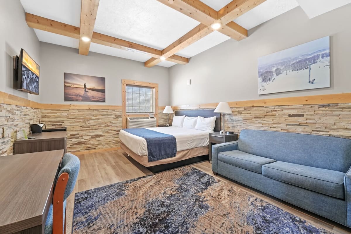 A bedroom with a bed, a blue sofa, a desk, and a stone wall.