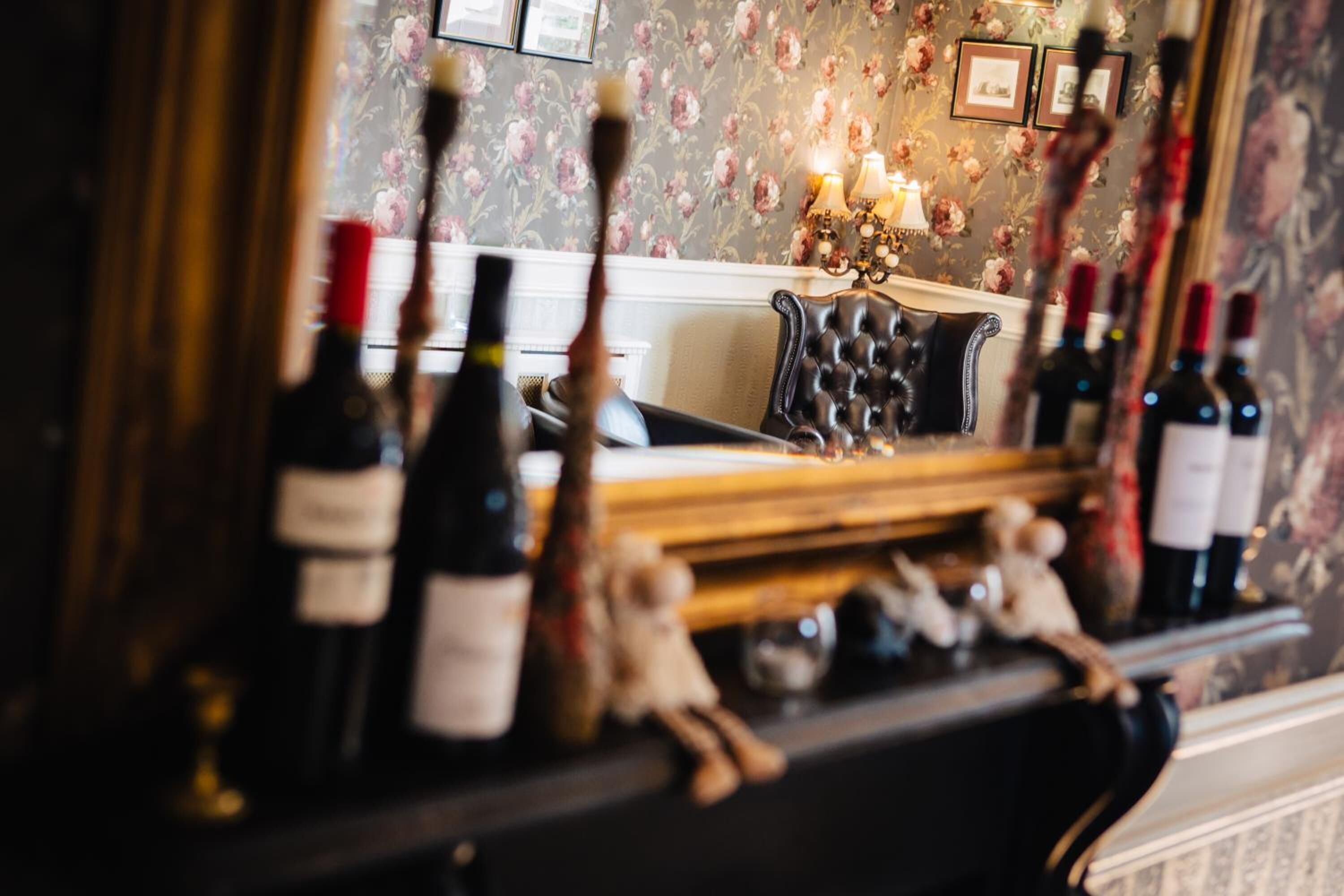 Zona de bar con un espejo que refleja el salón, una chimenea y botellas de vino.