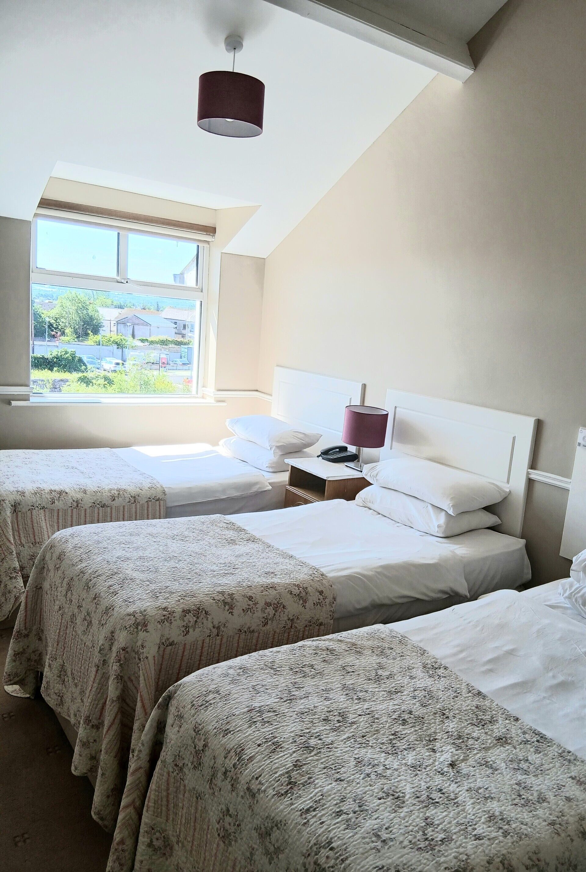A bedroom with two beds, a window, and a lamp.