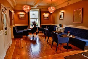 A room with wooden flooring, a blue sofa, black chairs, and a table with a vase. - Gleesons Restaurant & Rooms (Roscommon)