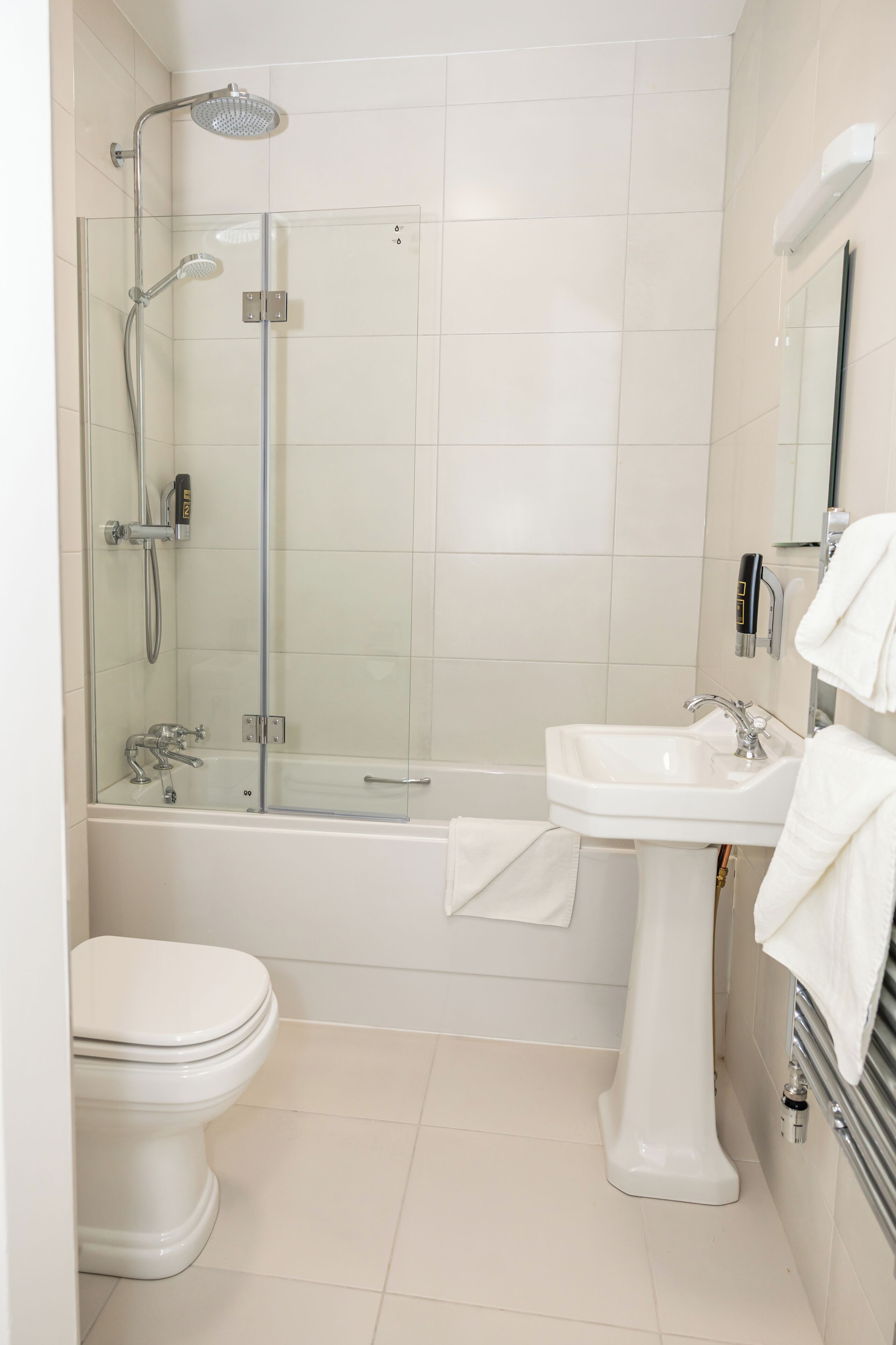 A modern bathroom with a glass-enclosed shower, a white pedestal sink, and a toilet.