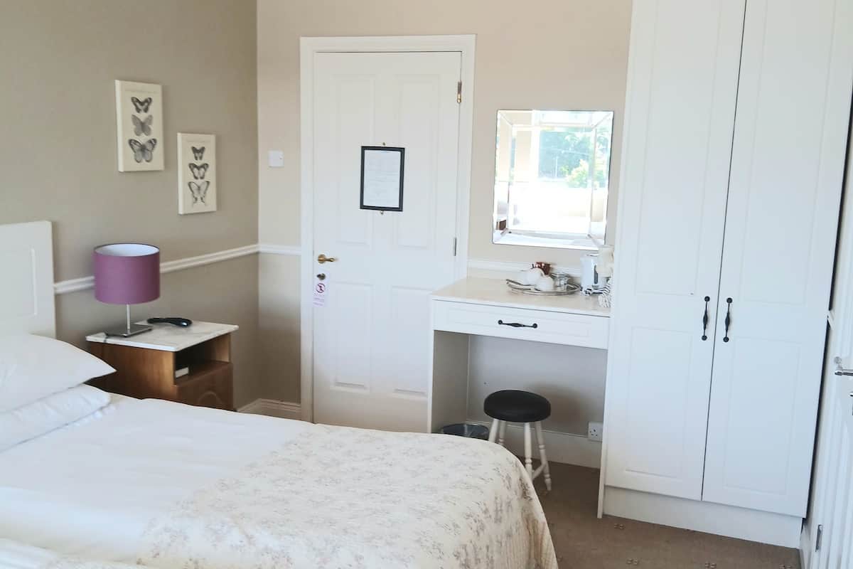 Quarto com duas camas, uma escrivaninha, um guarda-roupa e uma janela.