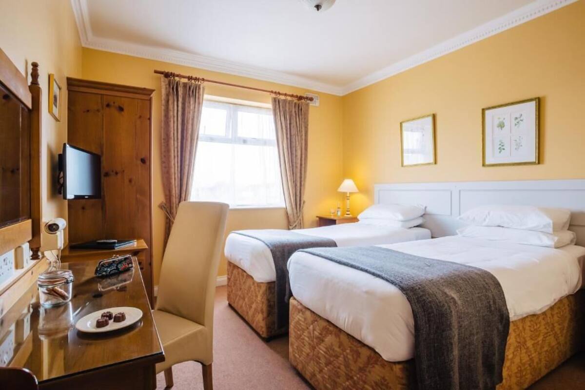 Quarto de hotel com duas camas, uma mesa de trabalho com cadeira, televisão e janela com cortinas.