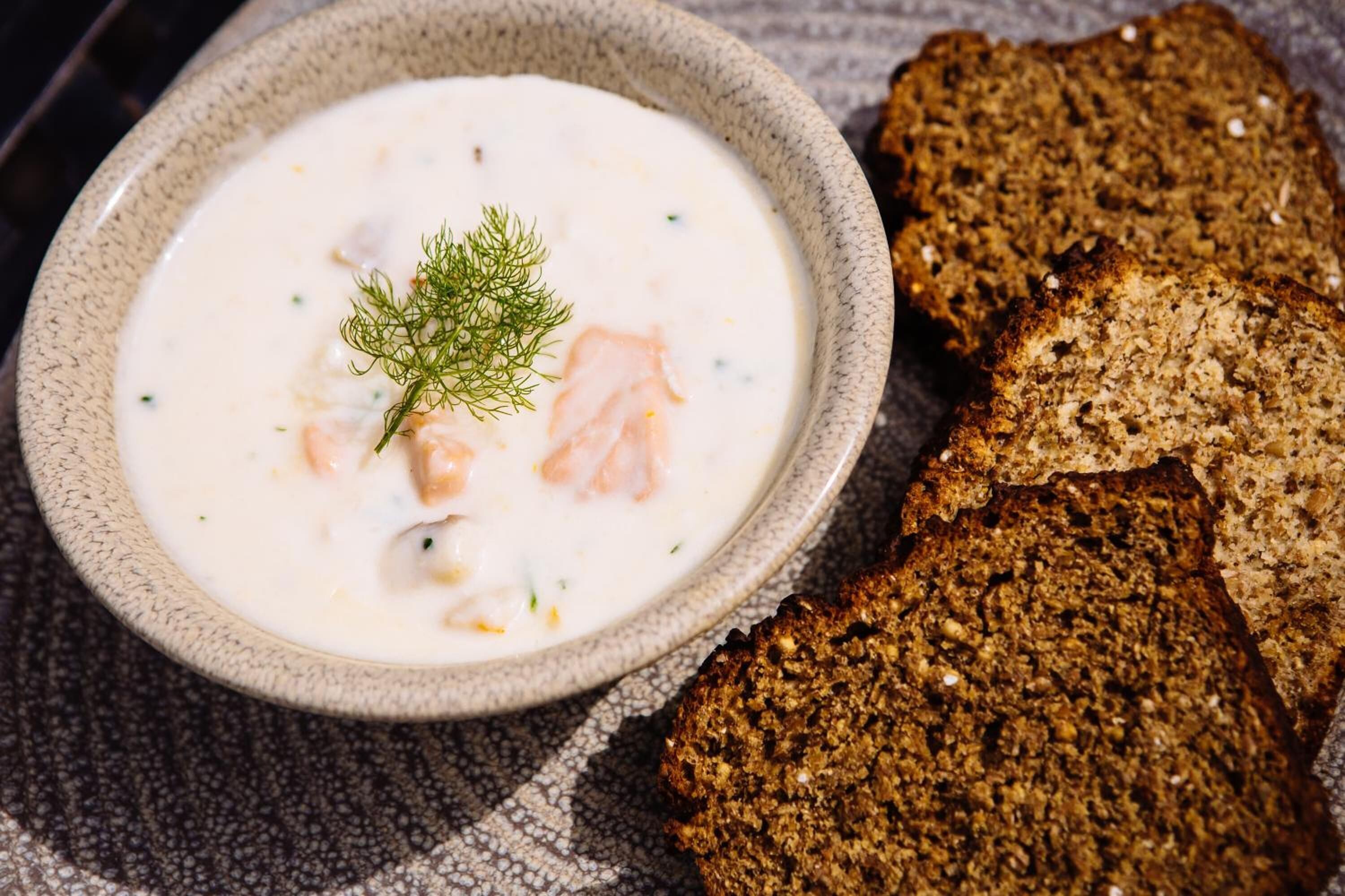 Un bol de soupe crémeuse au saumon, garnie d’aneth, accompagné de tranches de pain de seigle foncé.