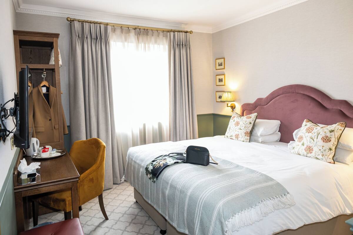Quarto de hotel com cama, escrivaninha, cadeira, guarda-roupa e janela com cortinas.