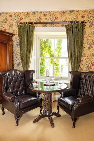 A room with two leather armchairs, a glass table, and a window with curtains.