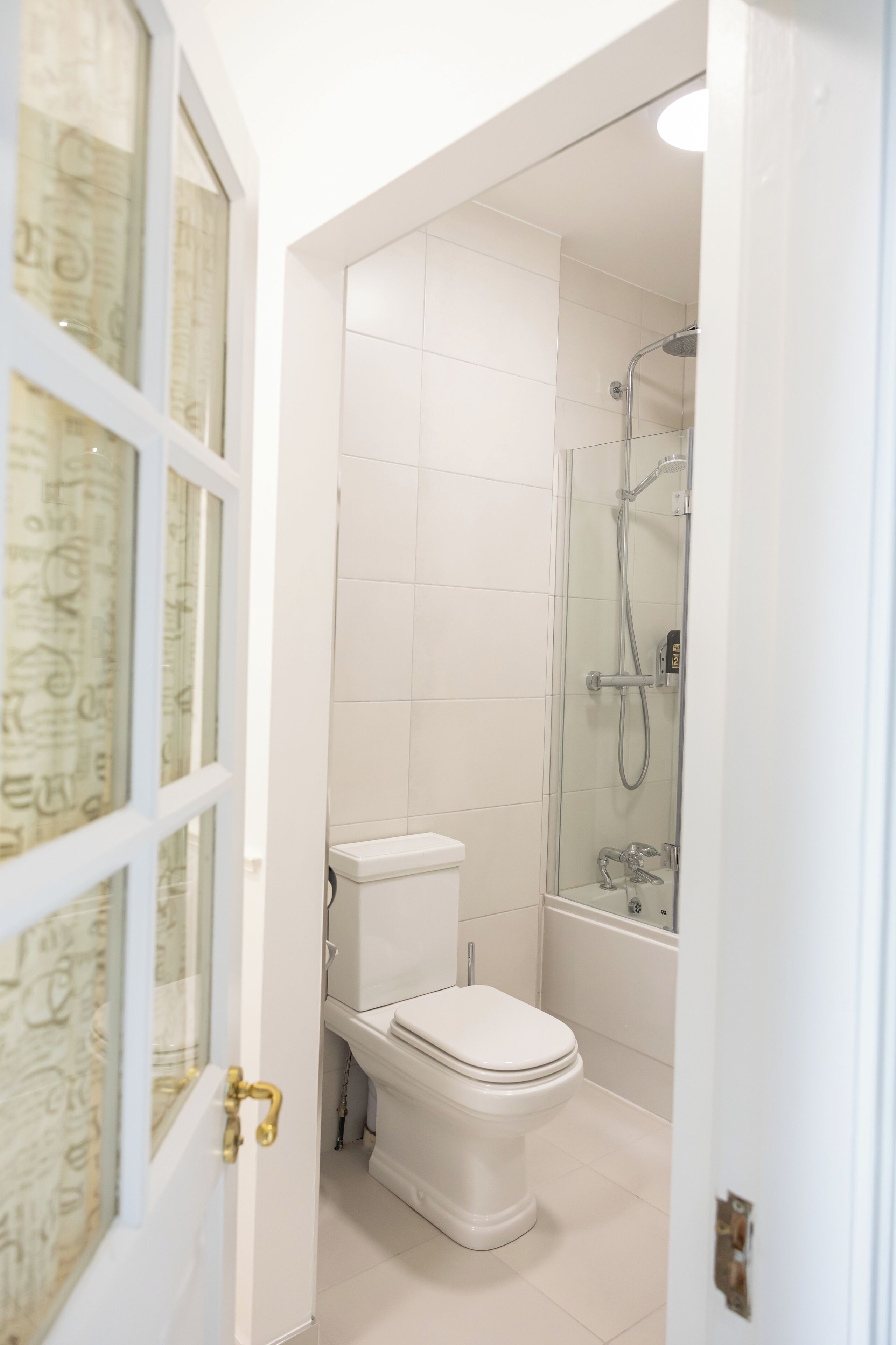 A bathroom with a toilet, shower, and a glass door leading to another room.