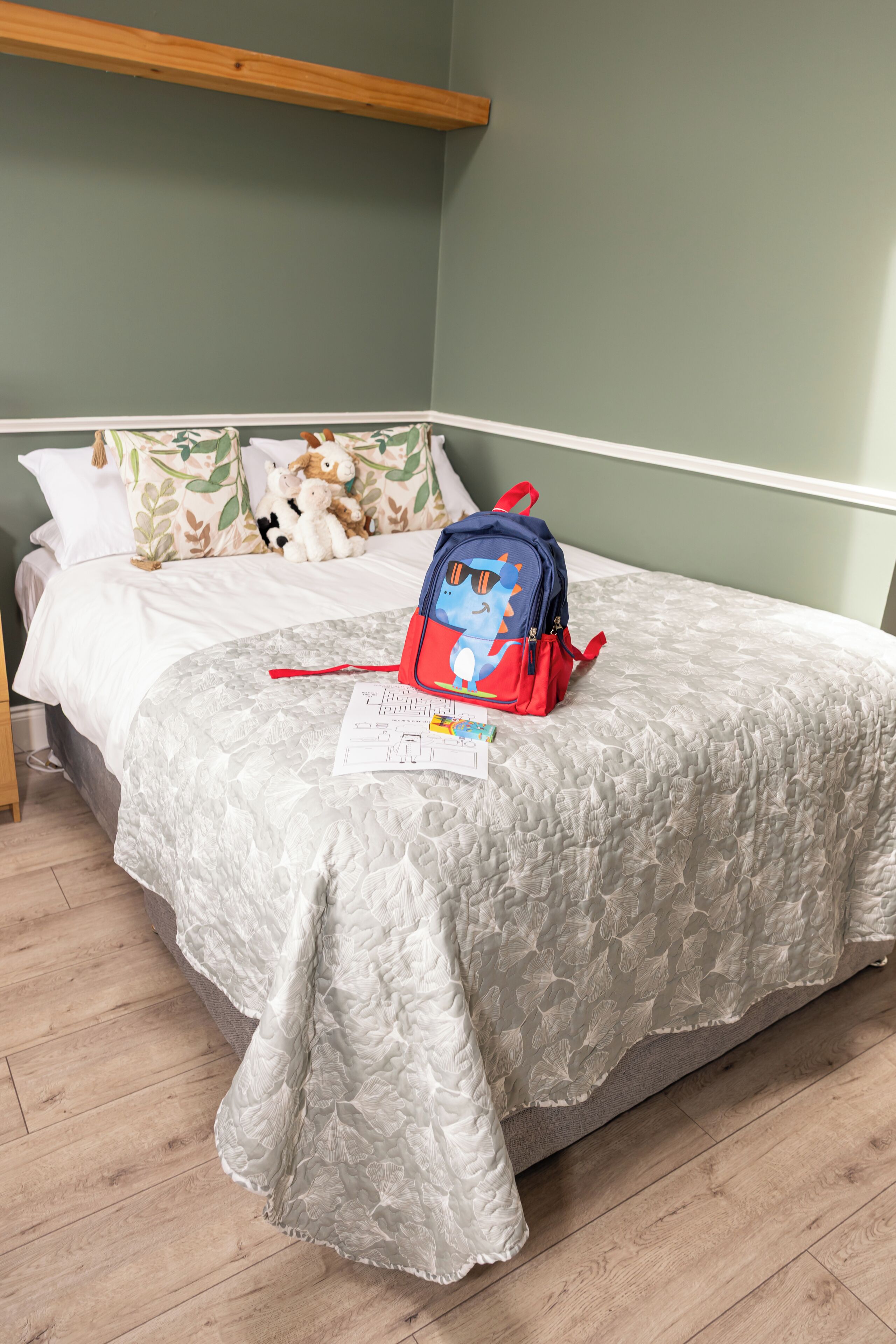 Une chambre à coucher avec un lit, un sac à dos bleu et un oreiller orné d’un motif de feuilles.