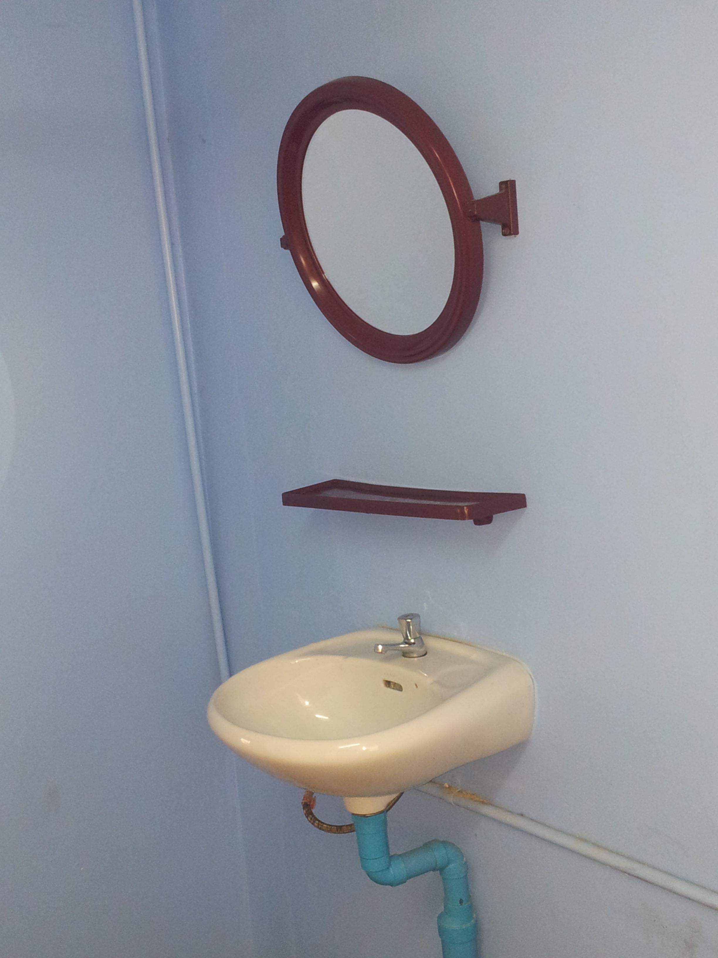 A bathroom with a white sink, a mirror, and a blue pipe.