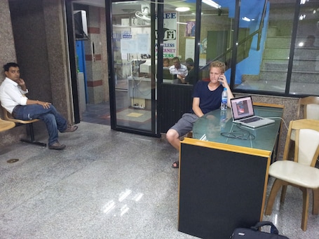 A waiting area with a glass partition, a laptop on a table, and a person sitting on a bench.