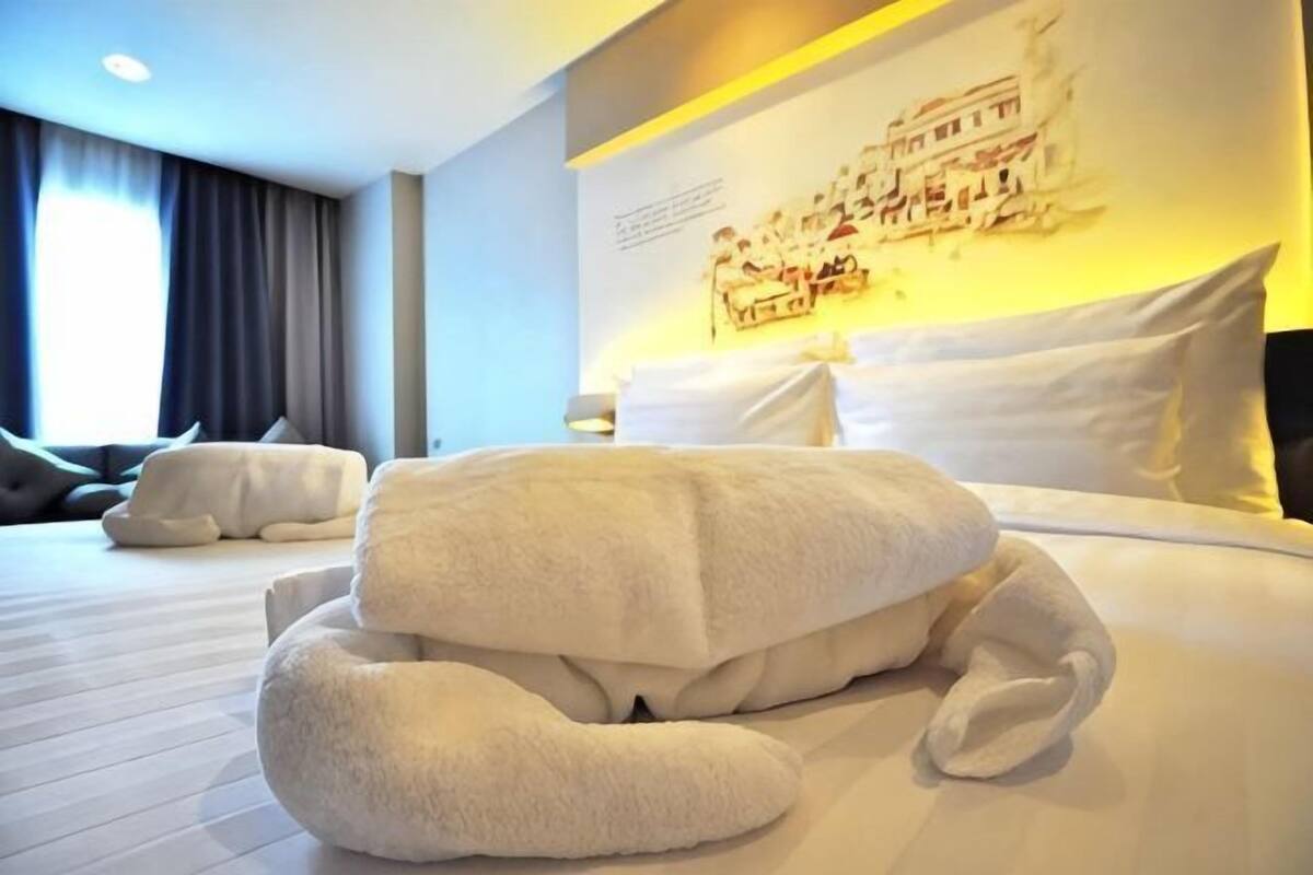 A hotel room with a neatly made bed, a large window with curtains, and a wall-mounted artwork.