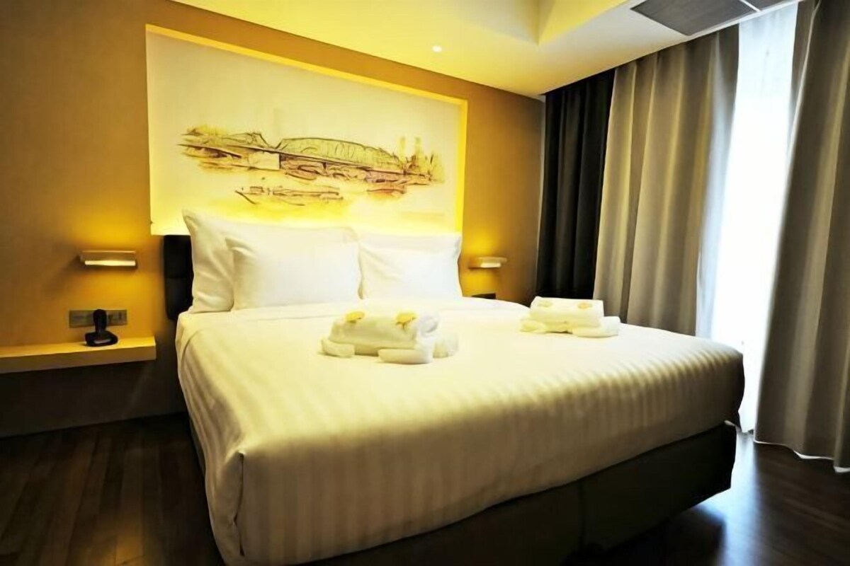 Habitació d'hotel amb un llit gran, dues làmpades de nit, un capçal de llit amb una obra d'art a la paret i una finestra amb cortines.