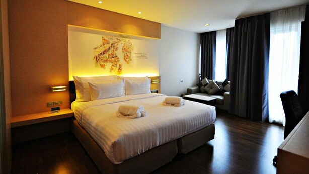 A hotel room with a large bed, a desk, and a chair. There is a map on the wall and a window with curtains. - Parinda Hotel (Bangkok)