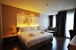 A hotel room with a large bed, a desk, and a chair. There is a map on the wall and a window with curtains. - Parinda Hotel (Bangkok)