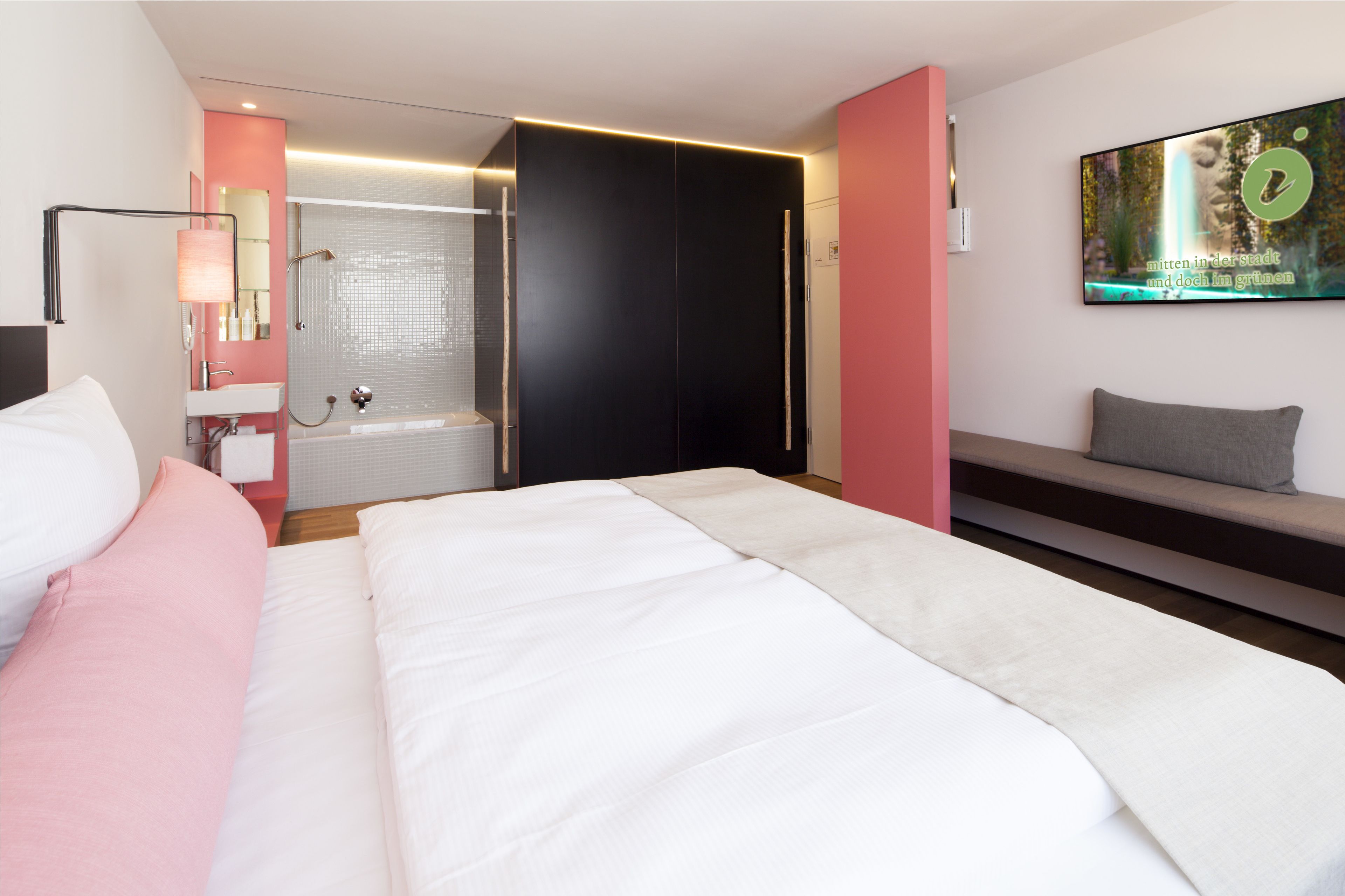 A modern hotel room with a large bed, a bathroom with a glass shower, and a painting on the wall.