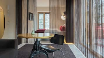 A modern room with a round table, a black chair, and a sofa. There is a window with curtains, a door, and a view of the outside.