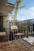 Un balcón con barandilla de metal, una silla de madera y plantas de bambú.
