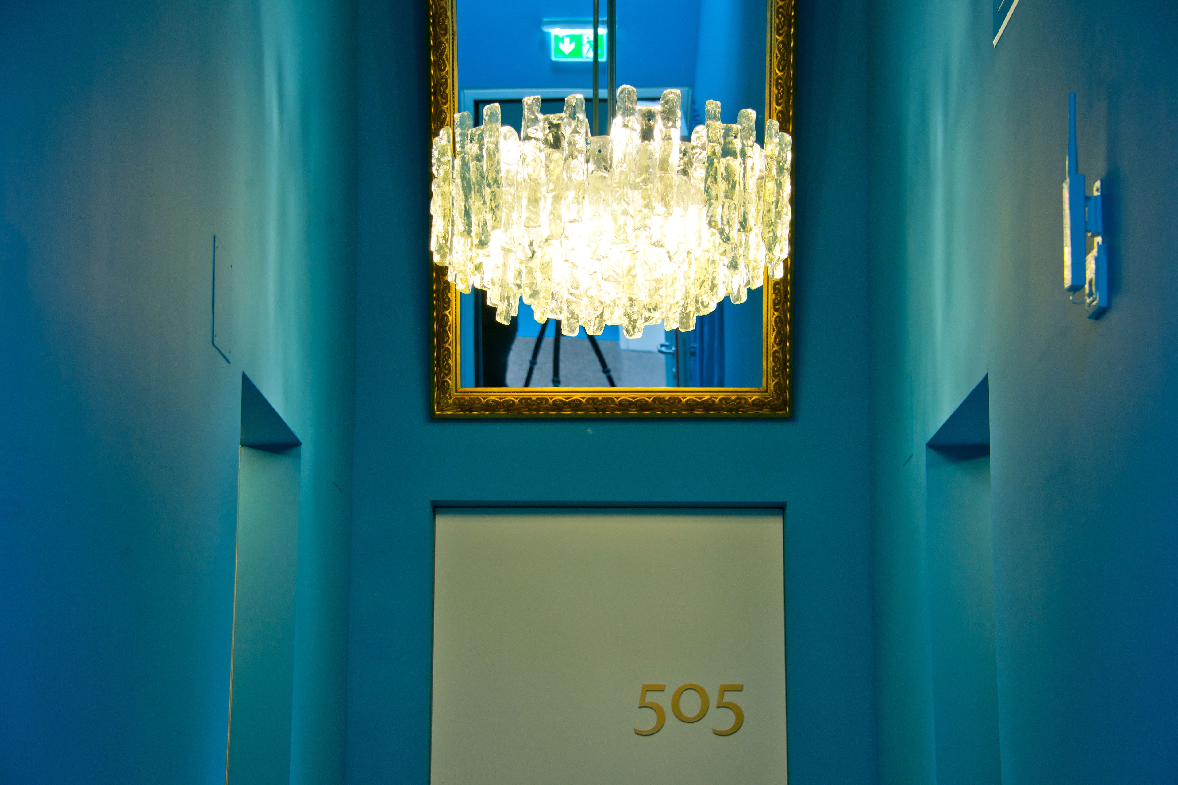 En blå gang med en lysekrone, et spejl og et skilt med nummer 505.