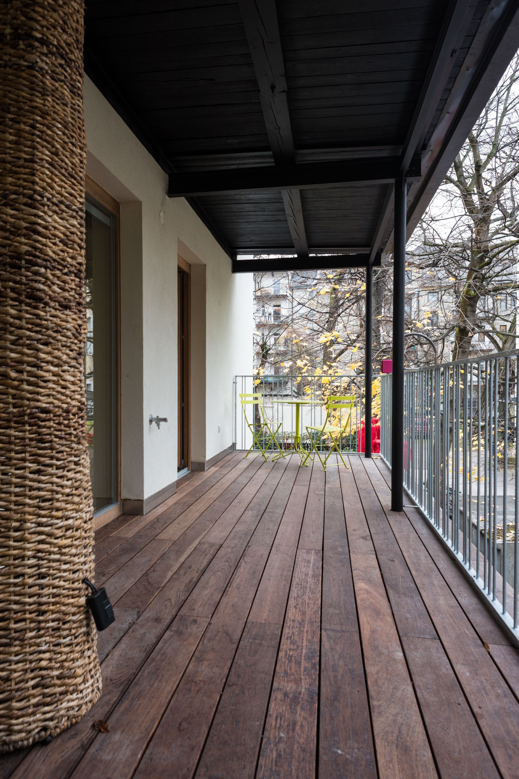 A wooden deck with a covered area, a wicker chair, and a metal fence.