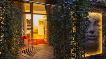 A wooden deck with a red bench, a glass door entrance, and a large illuminated sculpture.