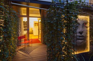 Una terraza de madera con un banco rojo, una puerta de cristal y una gran escultura iluminada.