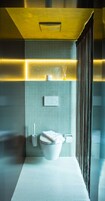 A modern bathroom with a white toilet, a towel rack, and a small shelf with a bottle and a candle.