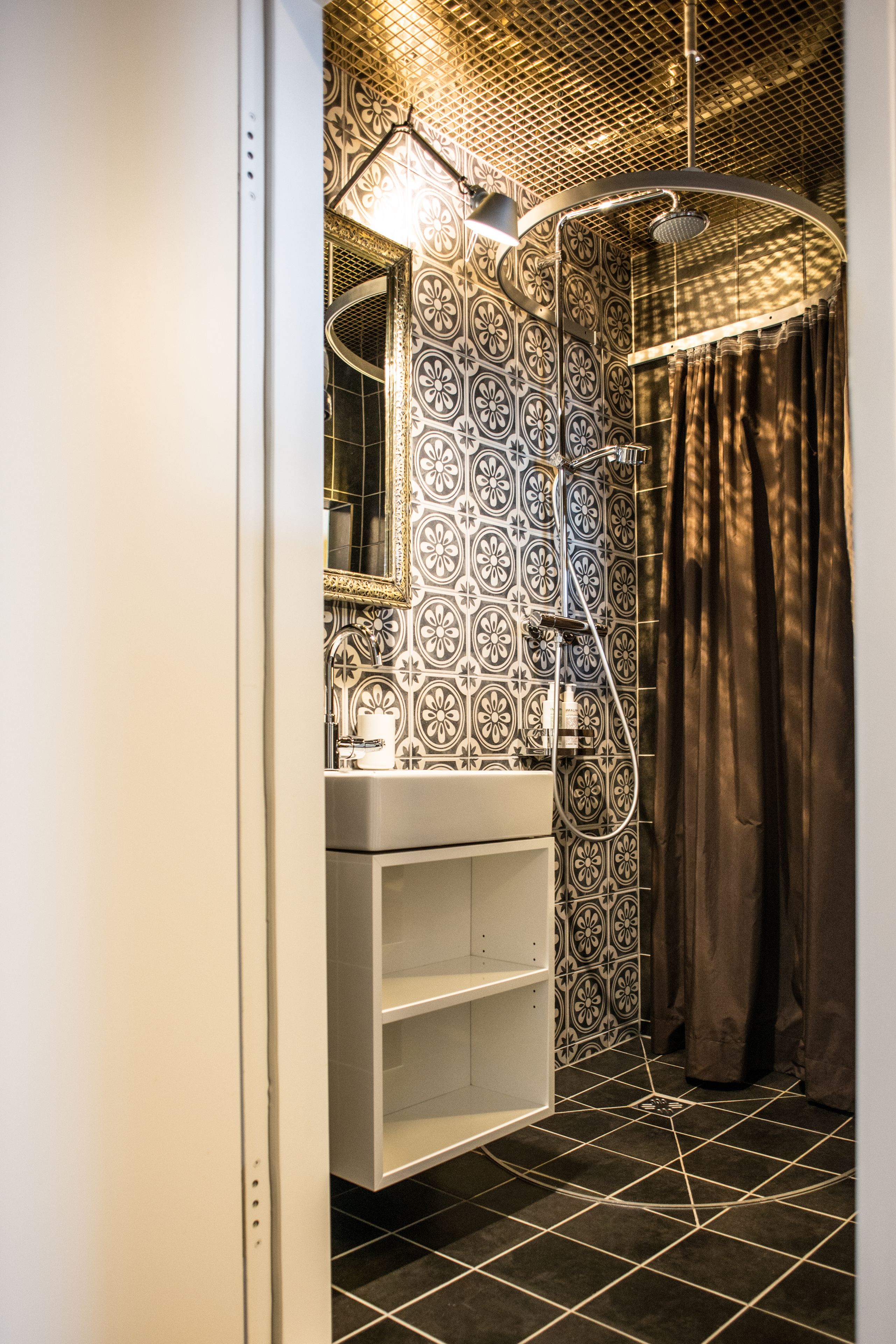 A bathroom with a patterned tile wall, a white sink, a mirror, and a shower with a curtain.