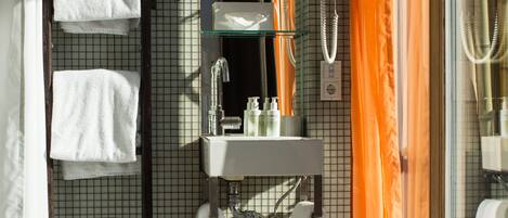 Un baño con pared de azulejos, repisas de vidrio con artículos de aseo, un lavamanos blanco y un perchero para toallas.
