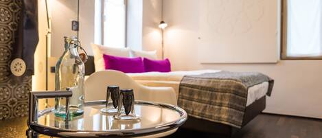 A modern room with a glass table, a bed with a purple pillow, and a large window.