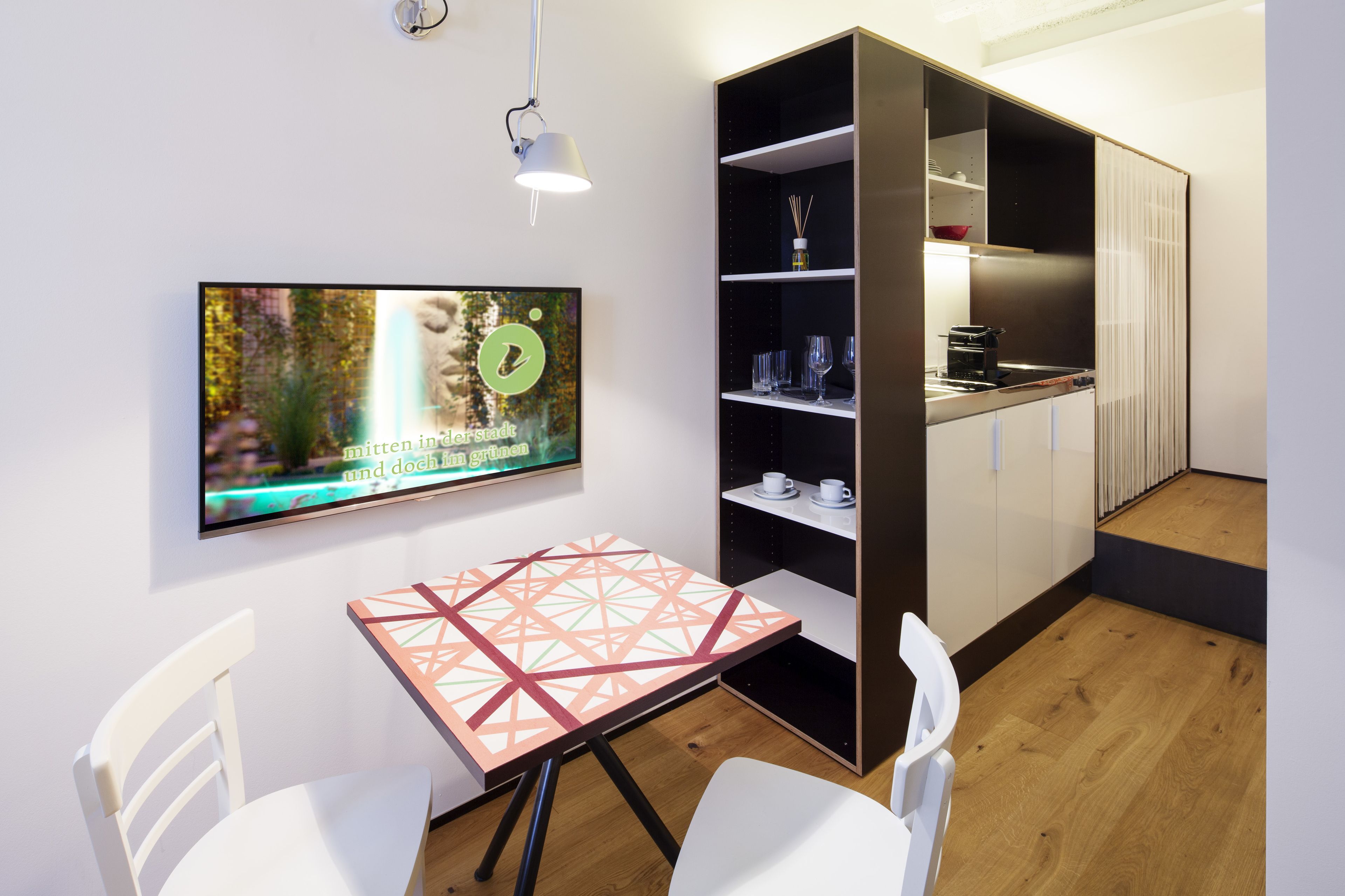 A modern kitchen with a built-in stove, a dining area with a table and chairs, and a wall-mounted TV displaying a nature scene.