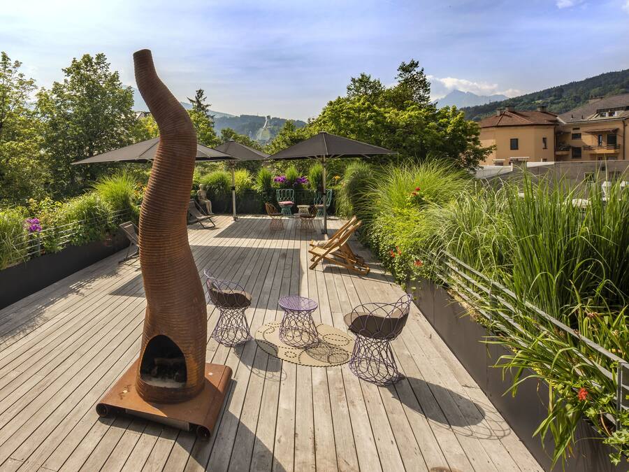 A wooden deck with outdoor furniture, a unique chimney-like structure, and lush greenery.