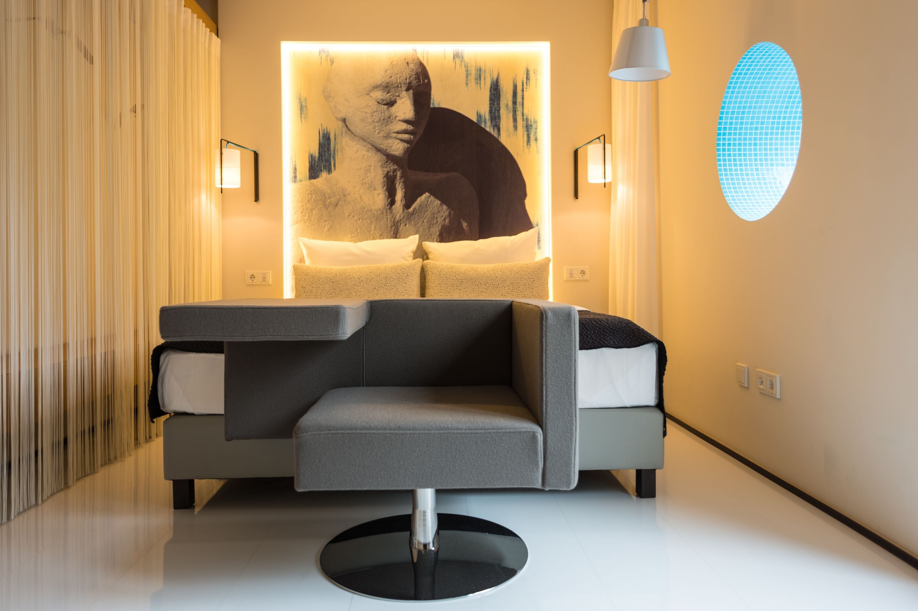 Une chambre moderne avec un canapé, un luminaire fixé au mur et un lustre original au plafond.