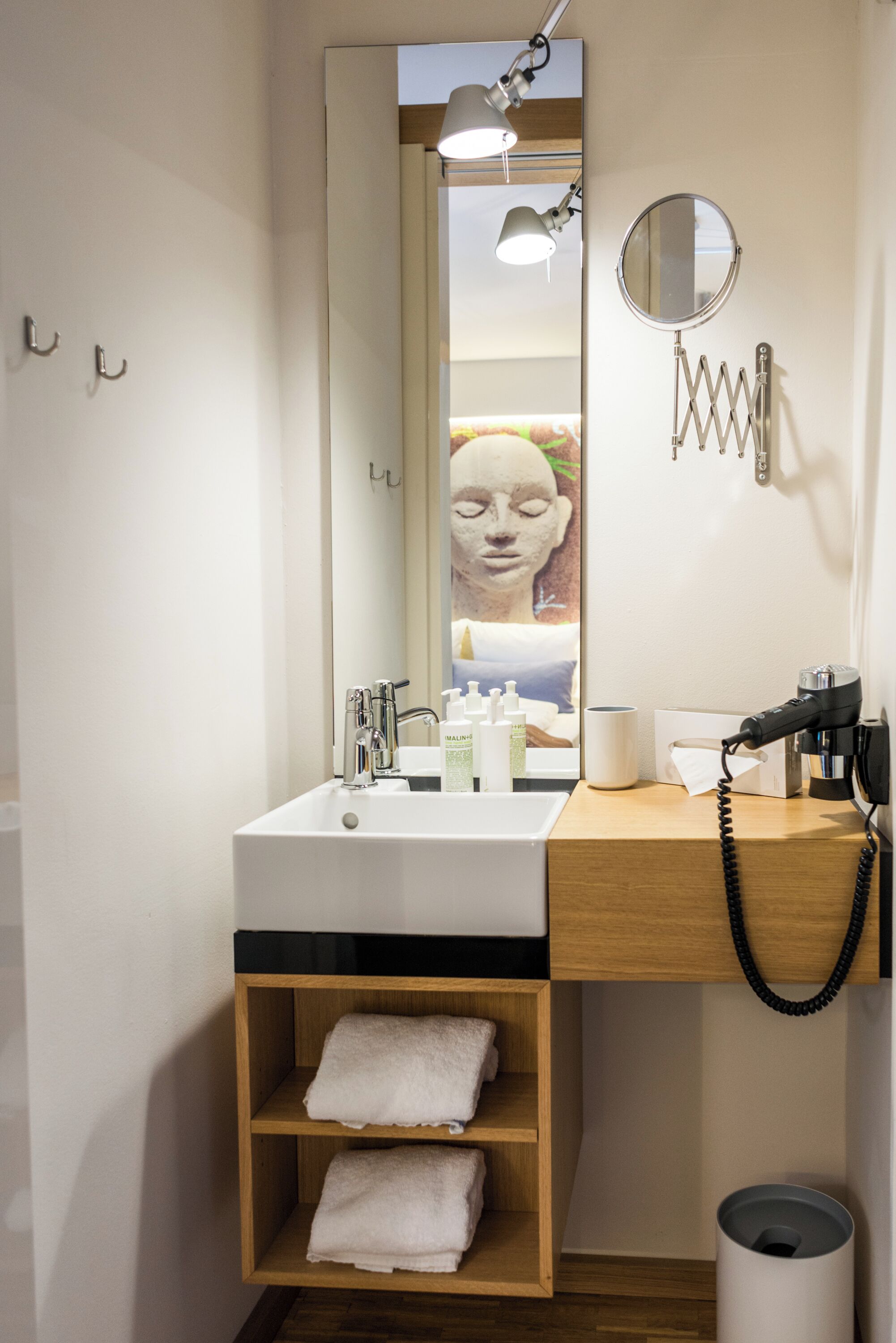 A modern bathroom with a large mirror, a sink, a hairdryer, and a towel rack.