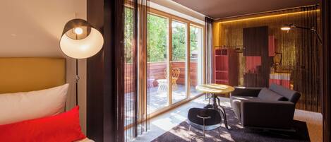 Habitación de hotel moderna con cama, sofá, una mesita y un ventanal que ofrece vistas al exterior.