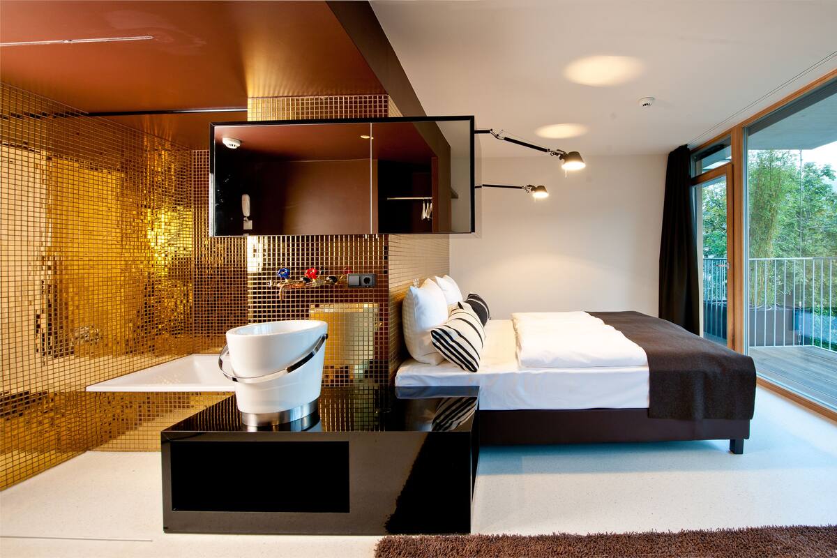 A modern bedroom with a large bed, a bedside table with a bowl, a mirror, and a view of the outdoors.