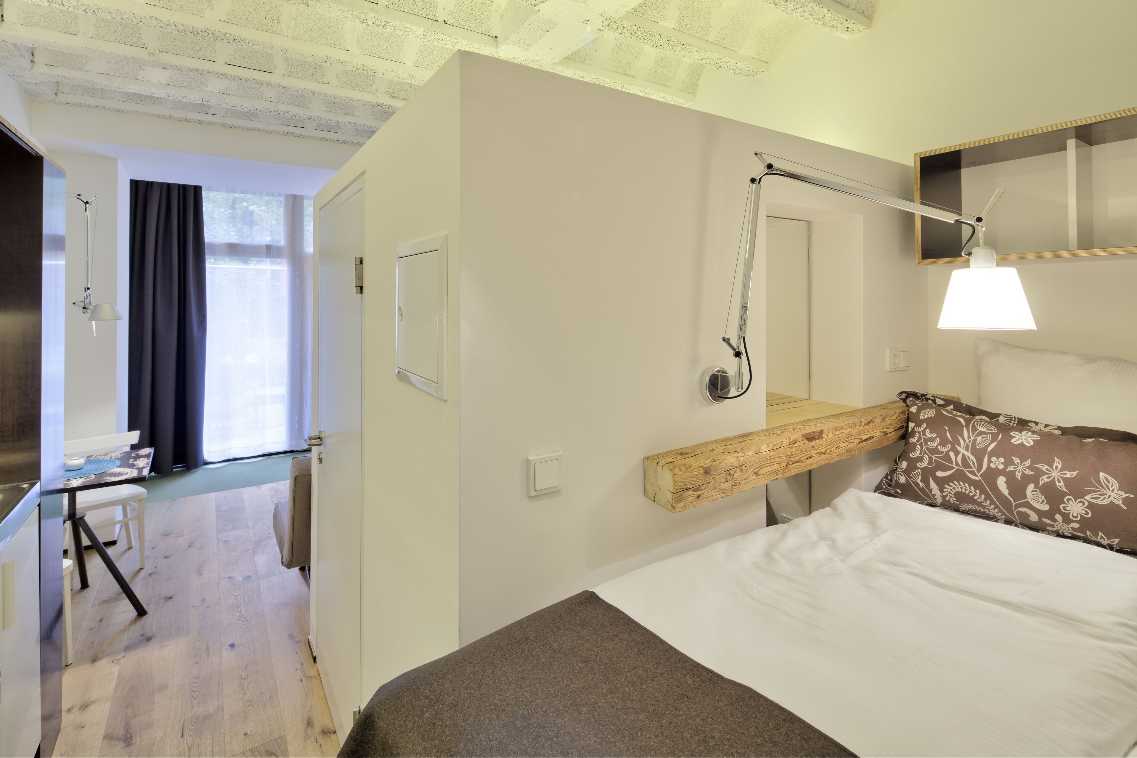 Un dormitorio con cama, mesita de noche, espejo y ventana con cortinas.