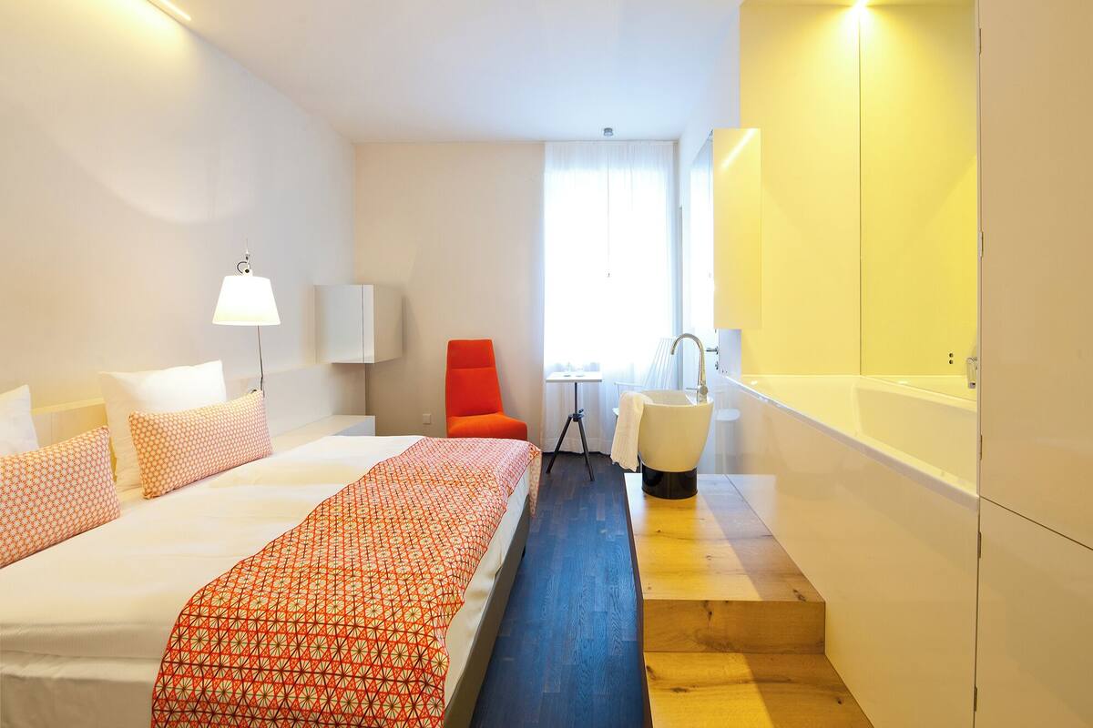 A hotel room with a bed, a chair, a sink, and a small table.