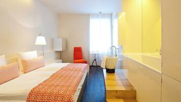 Una habitación de hotel con una cama, una silla, un lavabo y una mesita.