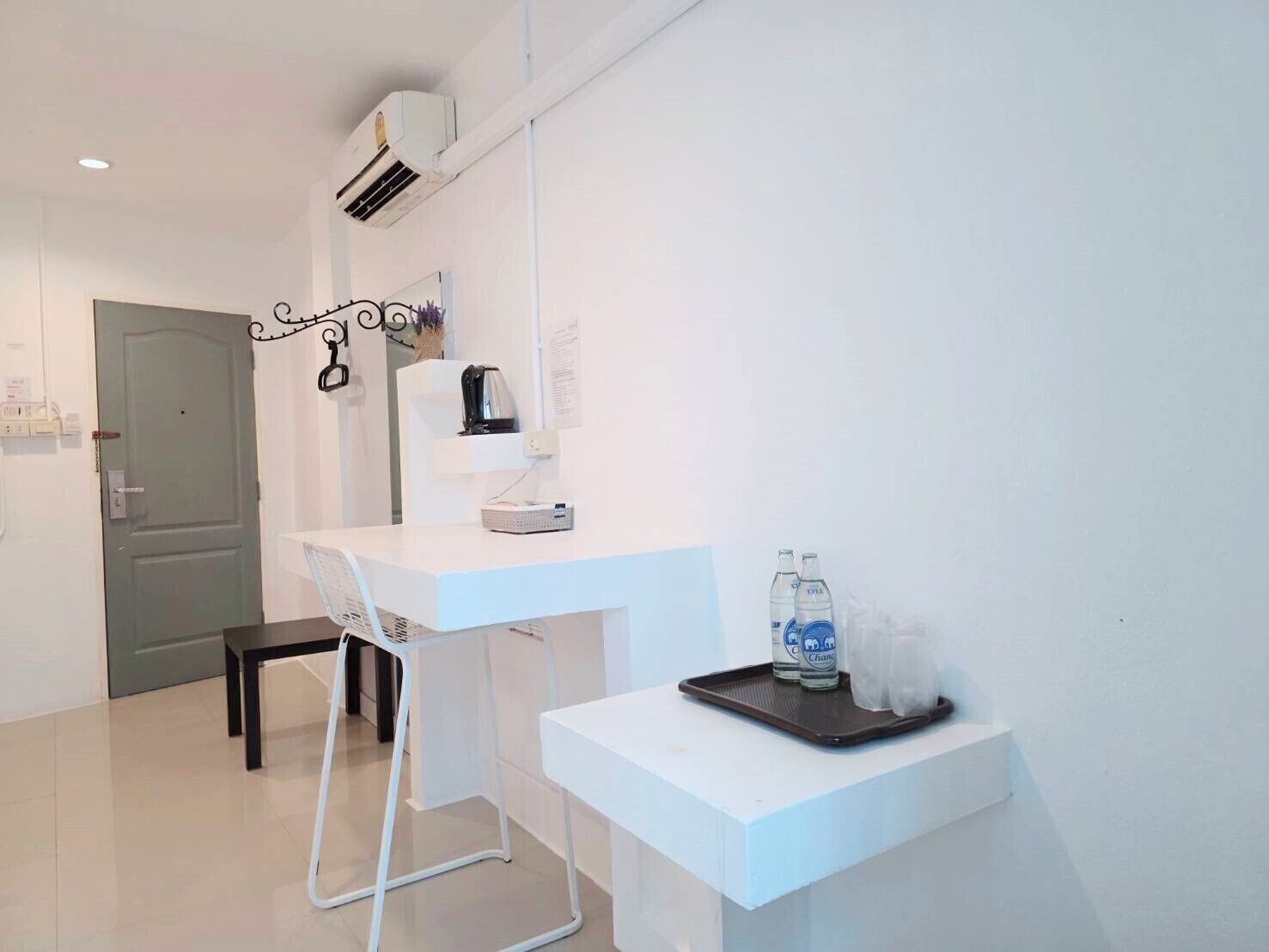 A modern, minimalist room with a white desk, a chair, and a small table with bottles and a tray.