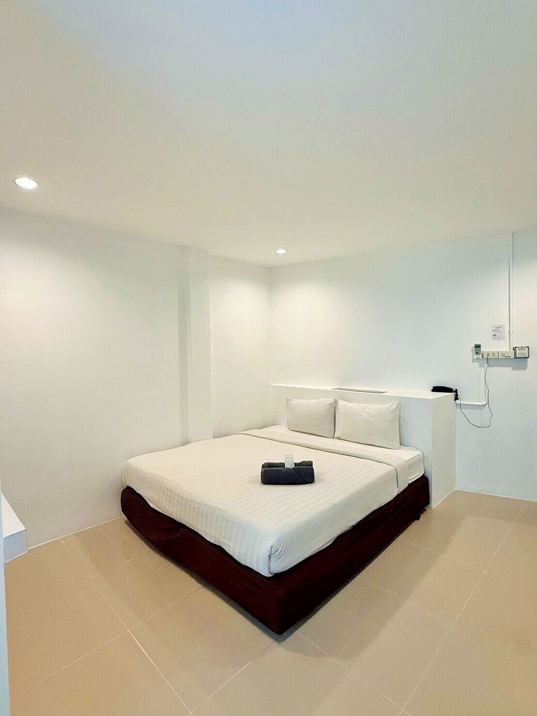 A minimalist hotel room with a large bed, white walls, and a tiled floor.